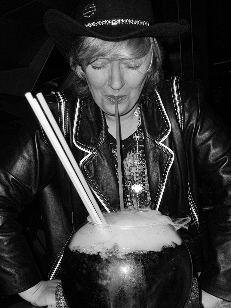 a woman in a black hat and leather jacket with straws in a large glass jar